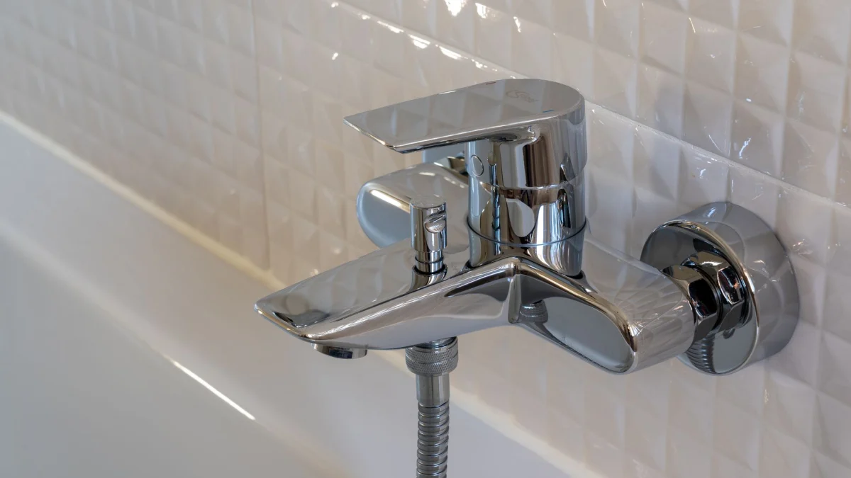 Close-up van een moderne chromen kraan in een eigentijdse badkamer met witte geometrische tegels.