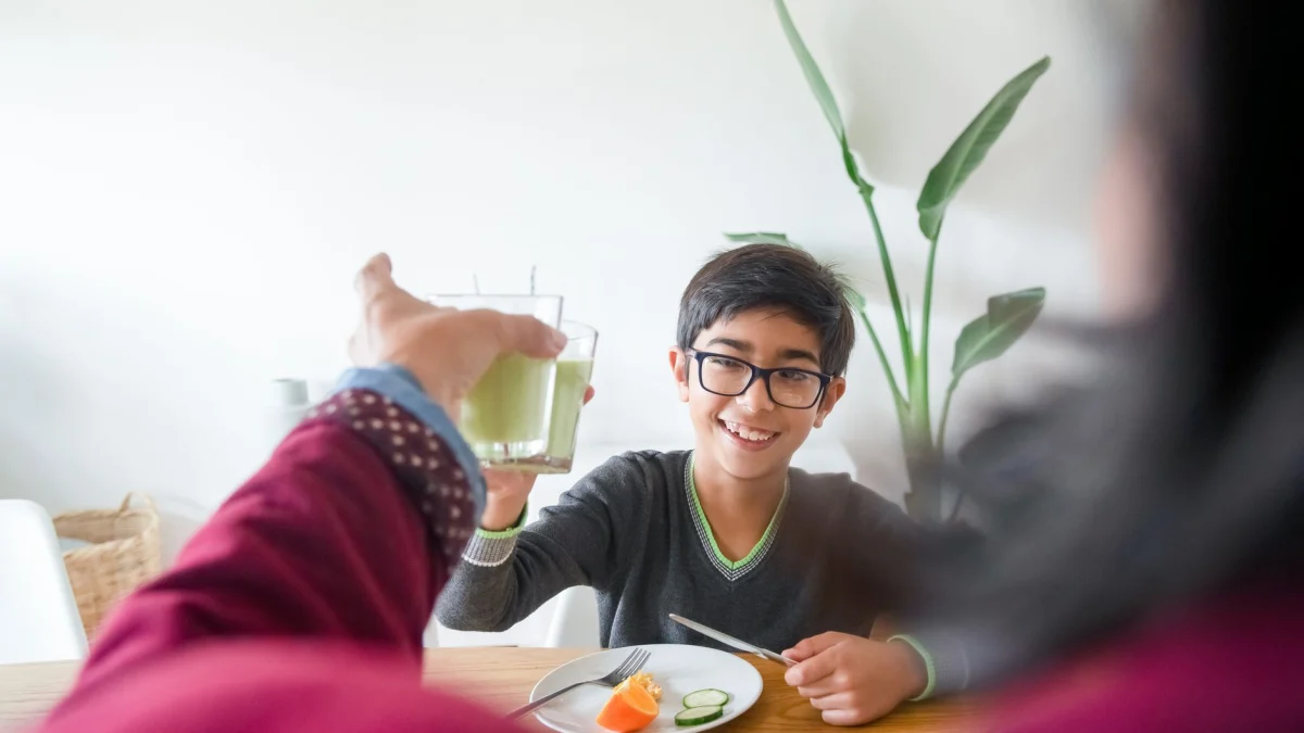 Gelukkige jongen die binnenshuis thuis ontbijt met sap.