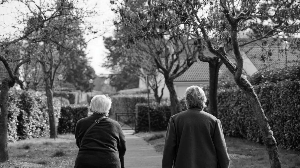 Zwart-witfoto van twee oudere volwassenen die overdag door een park wandelen.